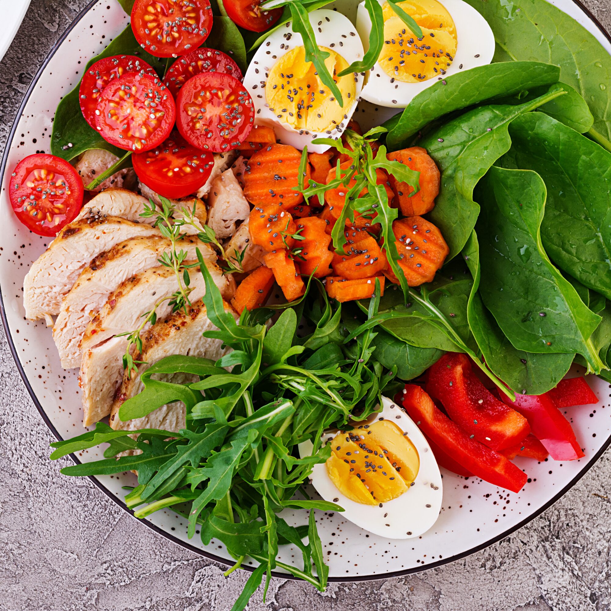 Plate with a keto diet food. Cherry tomatoes, chicken breast, eggs, carrot, salad with arugula  and spinach. Keto lunch. Top view